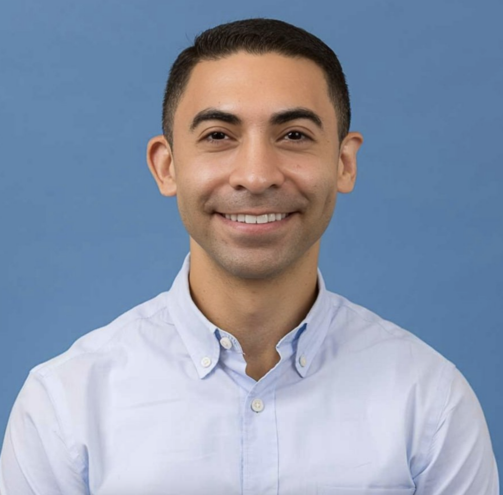 Jaime Castrellon smiling outdoors in a light blue collared shirt against a blue background.